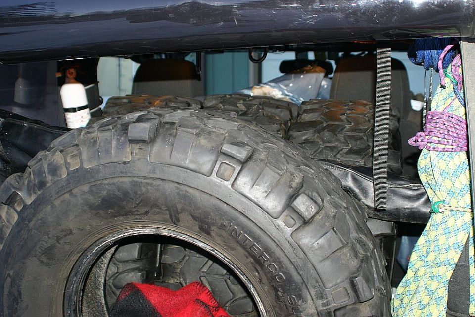 Spare tire with red blanket inside a vehicle, with ropes and a white cylinder visible