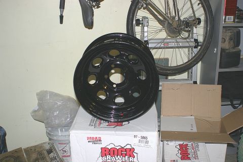 2003 Jeep TJ - A black steel wheel, possibly for off-roading, is displayed on top of product boxes.