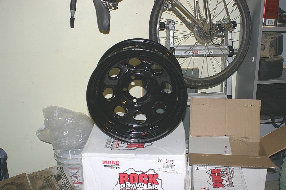 Black steel wheel labeled 'Rock Crawler' sits on top of boxes in a garage
