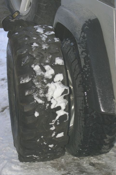 2003 Jeep TJ - A person is holding a large, snow-covered off-road tire next to a vehicle's wheel well.