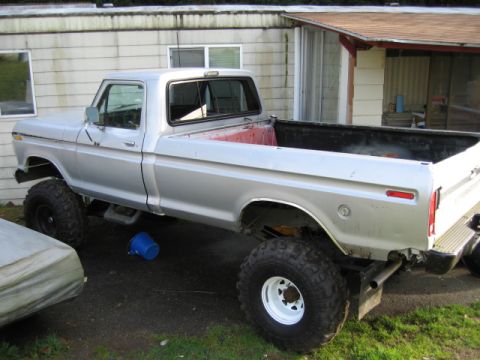 1976 Ford F-150 - This silver pickup truck, likely from the mid-1970s, is modified with a lifted suspension and oversized tires.