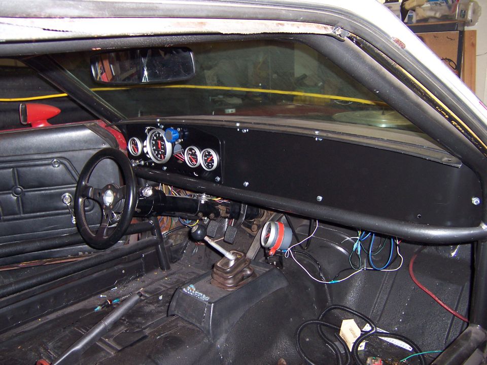 Stripped car interior with aluminum dash, aftermarket gauges, small steering wheel and roll bar