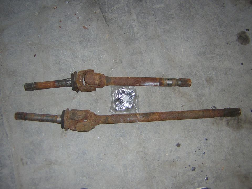 Two rusty drive shafts with universal joints and a small bag of hardware on a concrete floor