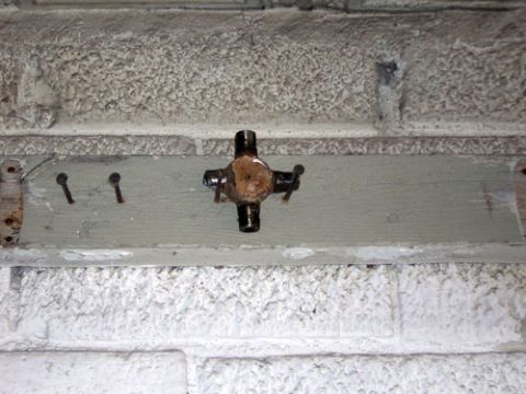 1995 Ford Bronco - A close-up view of a plumbing cross fitting secured to a painted wooden plank on a textured brick surface.