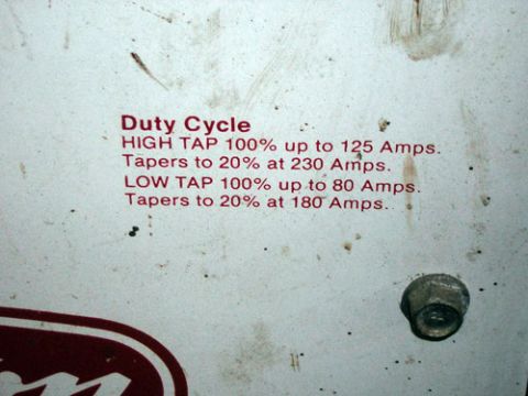 1995 Ford Bronco - Close-up of the red Duty Cycle text screened on a welder's scuffed white sheet-metal panel, reading HIGH TAP 100% up to 125 Amps, tapers to…
