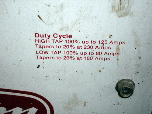 Duty cycle rating label in red text on a scuffed white welder panel