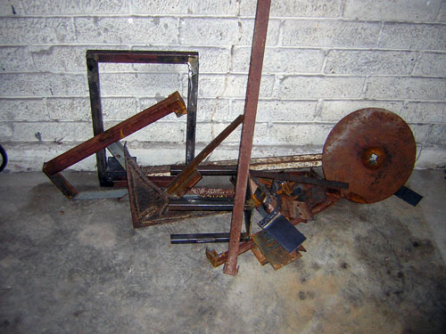 Rusty welded steel frame, tubing and a round disc stacked in a garage