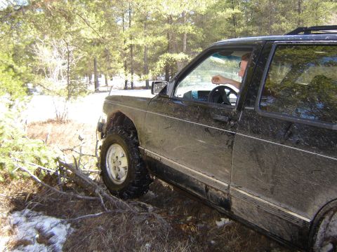 1978 Chevrolet C/K Pickup - A black SUV navigates a muddy, wooded trail with patches of snow.