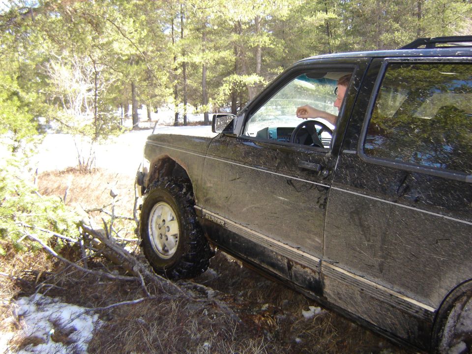 Black SUV with mud splatters, off-road tires, driving on a dirt path with trees and snow