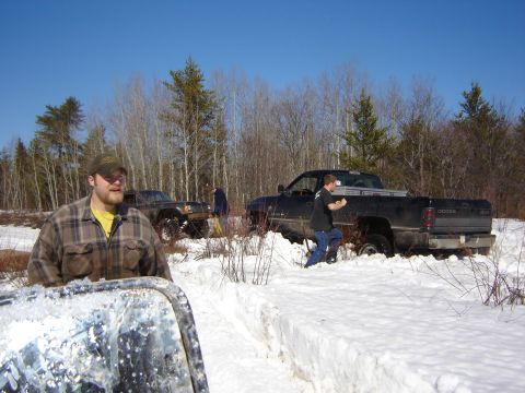 1978 Chevrolet C/K Pickup - Several people and vehicles are in a snowy, wooded area, with one truck stuck in a snowbank.