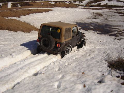 1978 Chevrolet C/K Pickup - A Jeep Wrangler navigates through deep snow, its rear tire visible as it struggles for traction.