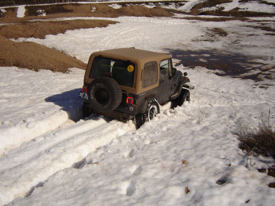 Dark Jeep Wrangler with tan top stuck in snow, rear view