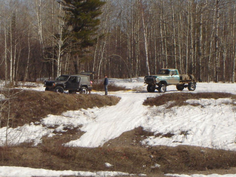 1978 Ford F-Series pickup truck and a dark SUV parked in a snowy, wooded area