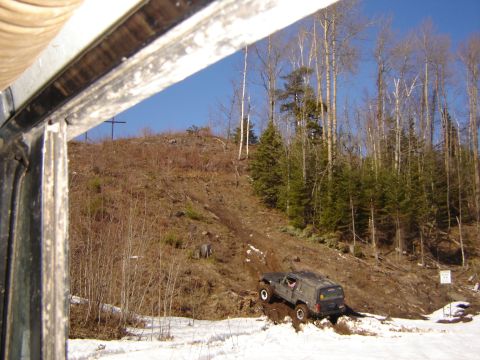 1978 Chevrolet C/K Pickup - A Jeep navigates a steep, muddy incline on a sunny day with snow patches visible.