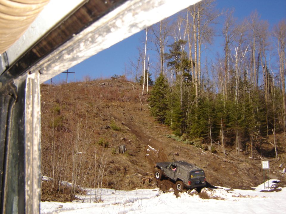Jeep Cherokee XJ climbing a muddy hill with trees and snow around