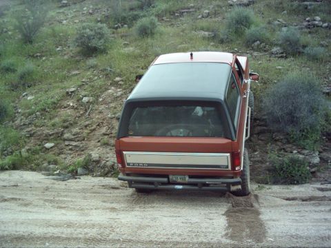 1988 Ford Bronco - This Ford Bronco is navigating a dirt trail with sparse vegetation on the hillsides.