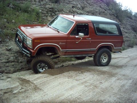1988 Ford Bronco - Lifted Ford Bronco navigating a dirt trail in a rocky, arid landscape.