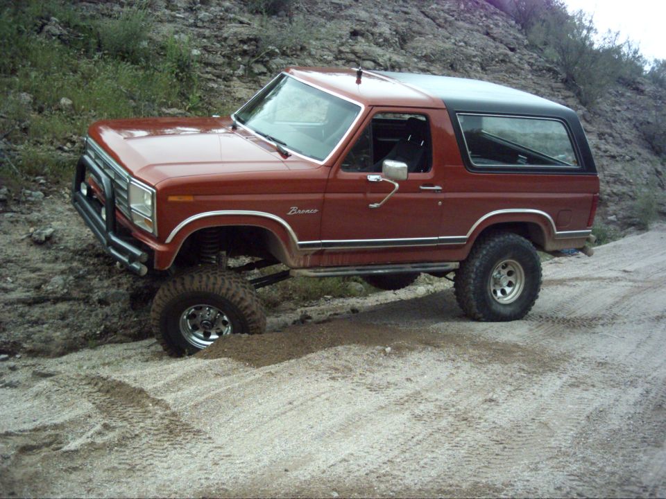 Red Ford Bronco with black top, lifted suspension, off-roading on a dirt path