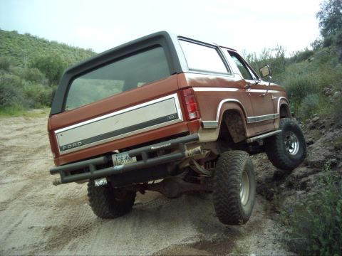 1988 Ford Bronco - This lifted Ford Bronco is navigating a steep, rocky incline on a dirt trail.