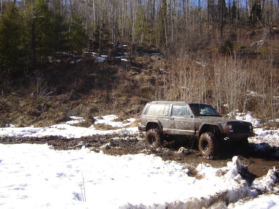 Muddy Jeep Cherokee XJ with large tires stuck in a snowy, muddy trail