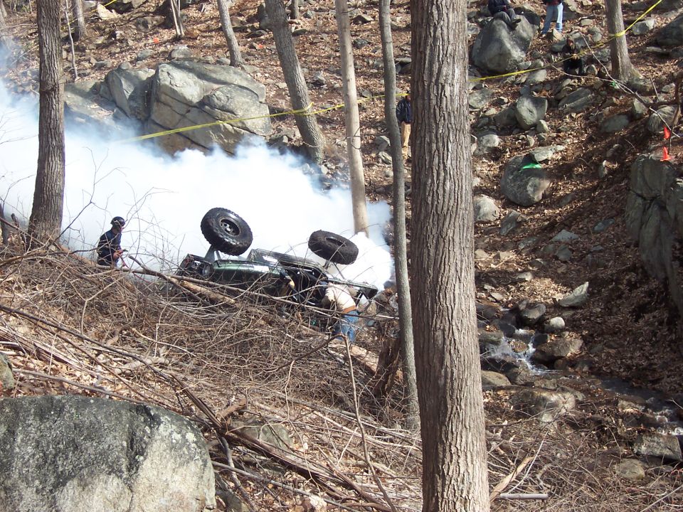 Off-road vehicle rolled onto its roof on a wooded slope with white smoke or dust rising