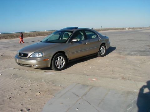 1997 Ford Taurus - A gold sedan is parked on a sandy lot with a person walking in the background.