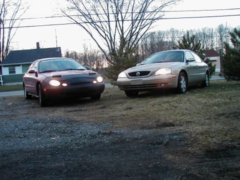 1997 Ford Taurus - Two sedans are parked outside on a grassy area with trees in the background.
