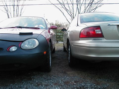 1997 Ford Taurus - Two sedans are parked closely together on a gravel surface, with bare trees in the background.