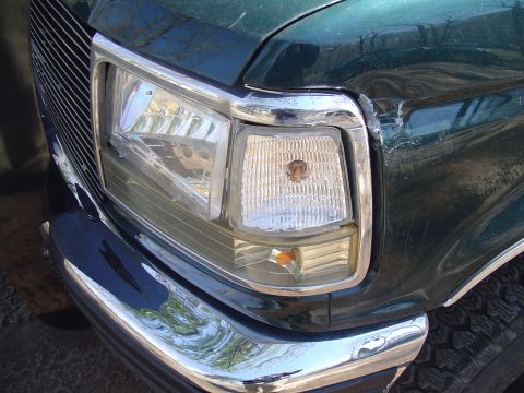 1993 Ford Bronco - Front corner of a green SUV, a chrome bumper, grille, and headlight assembly. The vehicle appears to be a 1992 model.