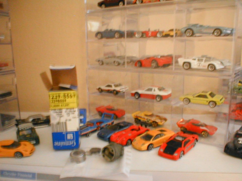 Collection of toy cars on shelves and a table, with a box of parts