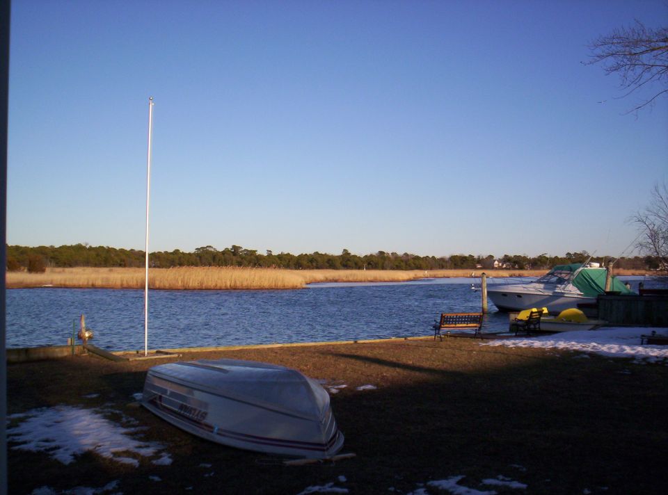 Overturned aluminum skiff on a waterfront lawn with a covered cabin cruiser at a dock