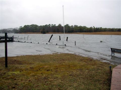 1995 Ford Bronco - Storm-flooded waterfront scene with choppy gray water covering a bulkhead and dock pilings, a park bench partly in the water, and a treelin…