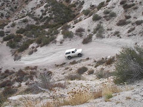 1988 Ford Bronco - A white 1987 Ford Bronco navigates a winding dirt road through a desolate, arid canyon.