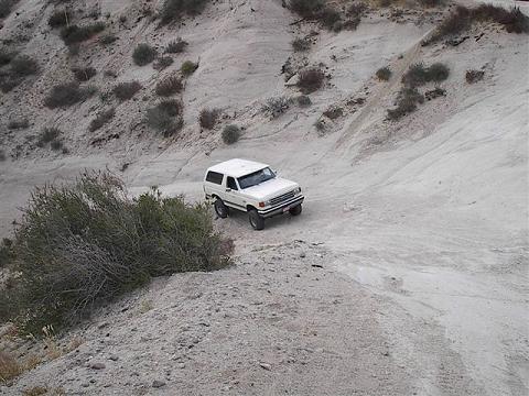 1988 Ford Bronco - A white SUV navigates a steep, dusty off-road trail with sparse vegetation on the hillsides.