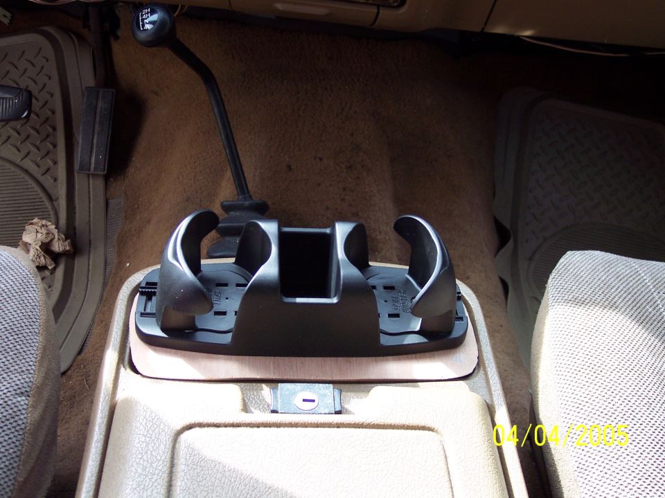 Black dual cup holder mounted on tan center console between seats, with shifter and 4WD lever visible