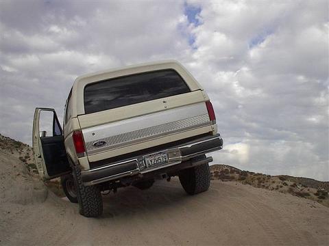 1988 Ford Bronco - This 1988 Ford Bronco is seen parked on a sandy slope, with its driver's door ajar under a cloudy sky.
