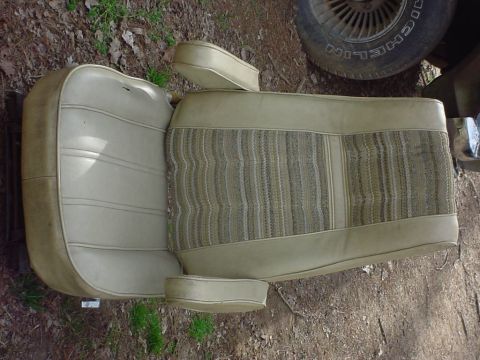 1979 Ford Bronco - A vehicle seat with tan vinyl and striped fabric is shown outdoors next to a tire.