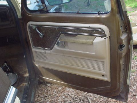 1979 Ford Bronco - Interior door panel of a 1979 Ford Bronco, showing the brown and tan trim and window crank.