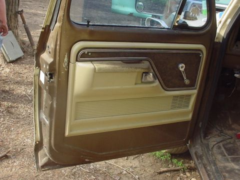 1979 Ford Bronco - The interior door panel of a 1979 Ford Bronco shows its brown and tan trim, with a manual window crank.