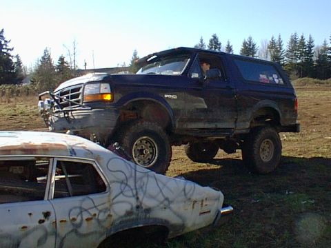 1995 Ford Bronco - A dark blue Ford Bronco is parked next to a damaged car in a field.
