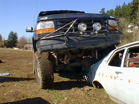 1995 Ford Bronco - A lifted 1995 Ford Bronco is parked next to a white car in a dirt lot.