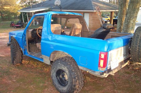 1987 Ford Bronco - This blue 1987 Ford Bronco is missing its doors and roof, showing its interior and custom modifications.