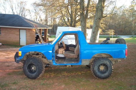 1987 Ford Bronco - Side view of a blue 1987 Ford Bronco with its doors off, parked outdoors.