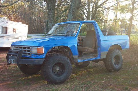 1987 Ford Bronco - This blue SUV, likely from the early 1980s, is modified for off-road use with large tires and no doors.