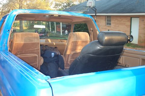 1987 Ford Bronco - The interior of a blue Ford Bronco is visible, with brown fabric seats and a black leather seat in the foreground.