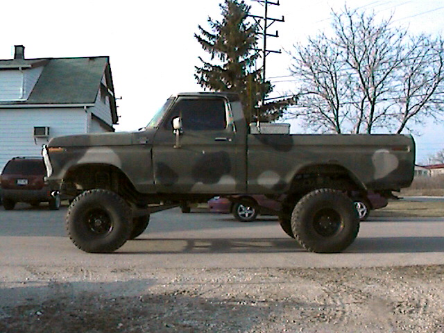 Lifted 1970s Ford pickup with camouflage paint and large mud tires on a street