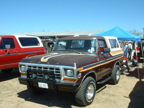 1978 Ford Bronco - A brown 1978 Ford Bronco with a white camper shell is parked next to a red Bronco under a blue tent.