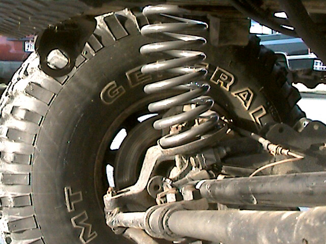 Close-up of front coil spring suspension and General MT tire under a lifted pickup