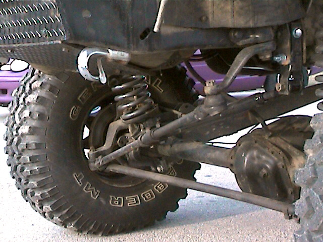 Front suspension close-up of lifted truck with coil spring, solid axle, tow hook, and General Grabber MT tire