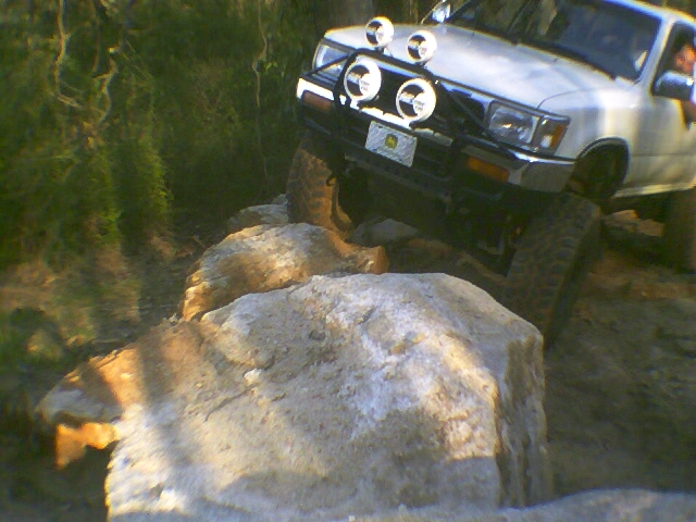 White lifted 4x4 truck with brush guard and round lights climbing a boulder on a trail